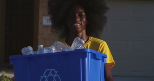 African American adolescents with huge Afro smiling as he hold recycle bin full of plastic bottles