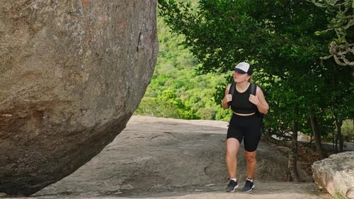 Active Woman Hikes Up Mountain Trail By Massive Rock Geared with Backpack for Adventure Climb Female