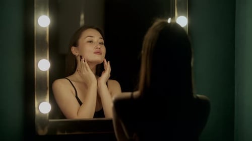 Woman Applying Lotion to Face in Front of Mirror
