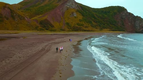 People Walking on Sandy Beach With Mountains