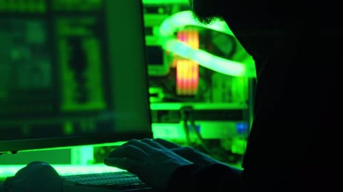 Man in a Hoodie is Hacking on a Computer in a Dark Room