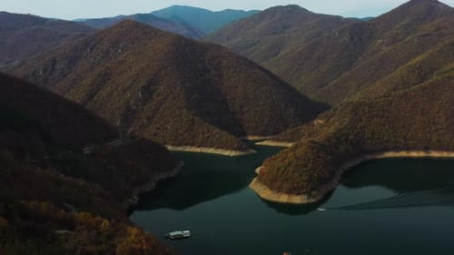 Flying over a lake in the mountains with moving boat in the water
