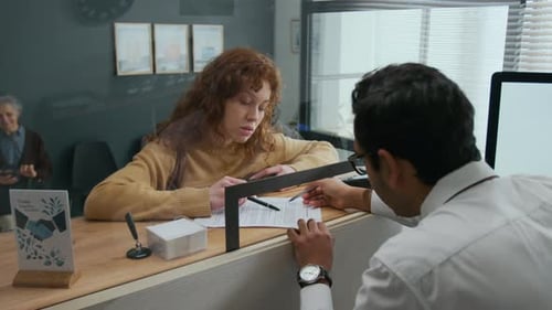 Young Woman Reviewing Document with Bank Teller in Office