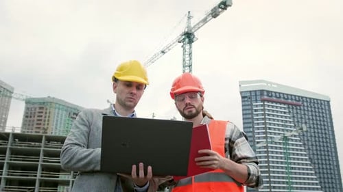 General Contractor and Subcontractor Using Laptop During Site Inspection