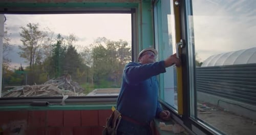 Worker using level tool to ensure window frame alignment at construction site, close-up of focused