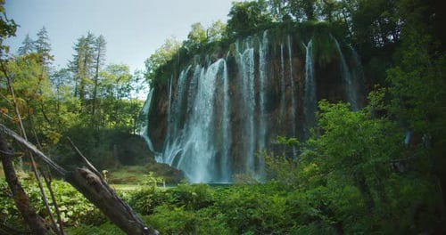 Massive Waterfall Plunges From Tall Cliff Into Lush Valley Surrounded By Trees