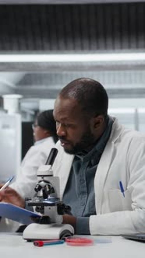 Scientist Using Microscope and Taking Notes in Lab