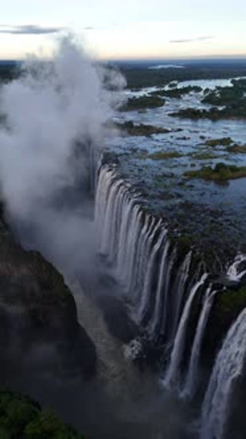Aerial view of Victoria Falls with powerful waterfall plunging into gorge, mist rising above lush