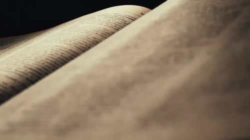 Hand dramatically turns page in old book in dark room, close-up