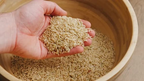 Hand Sifting Brown Rice in a Wooden Bowl