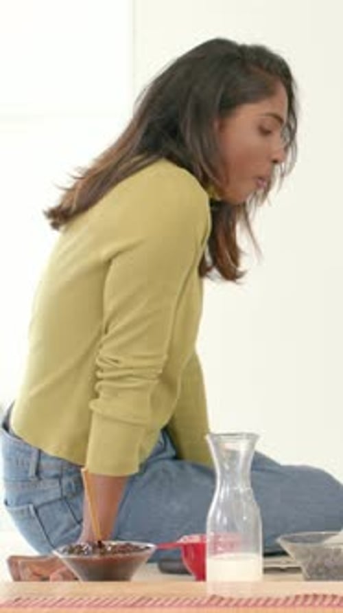 Vertical video: Shifting weight, woman scooping berries pouring milk for home breakfast, copy space