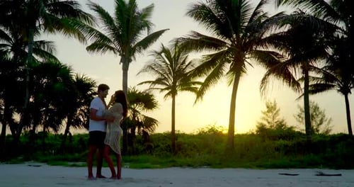 Romantic couple embracing on tropical beach at sunset with palm trees on vacation
