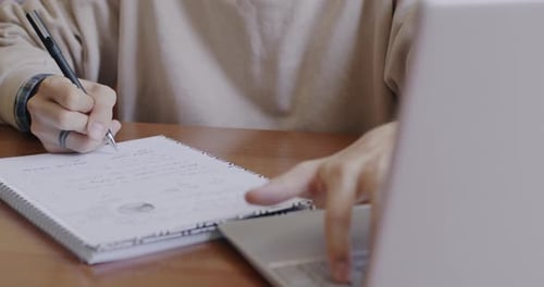 Closeup of Male Hand Writing in Notebook and Working with Laptop While Person Studying on Campus