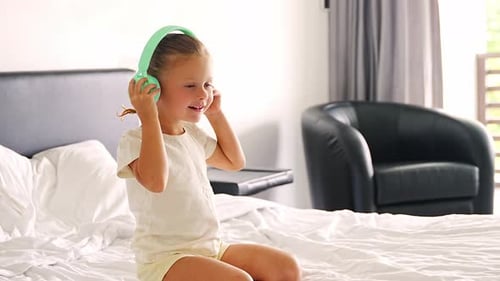 Little Girl Listening Music Using Green Kids Headphones in Home Bed