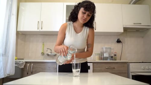 Young Woman Pours and Drinks Glass of Water