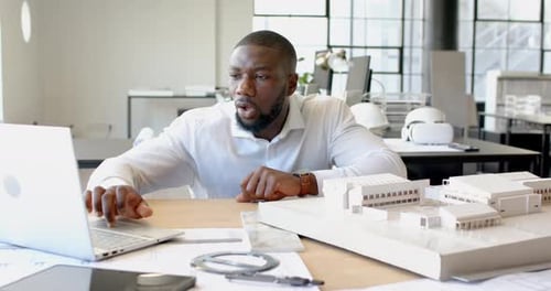 Smiling African American businessman working on laptop with architectural model in office