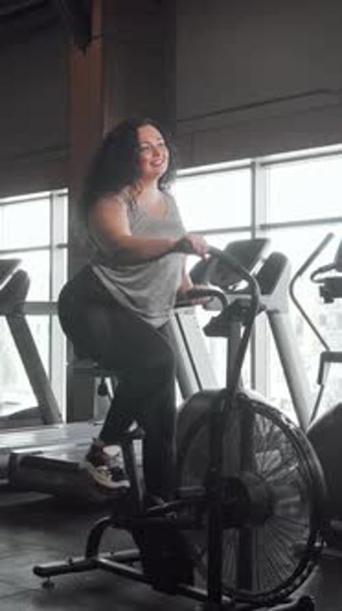 Joyeuse femme de grande taille faisant du vélo à air dans une salle de sport lumineuse