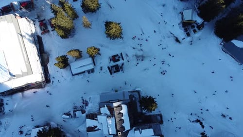 Static top down aerial clip of a busy mountain ski resort with skiers and snowboarders passing by am