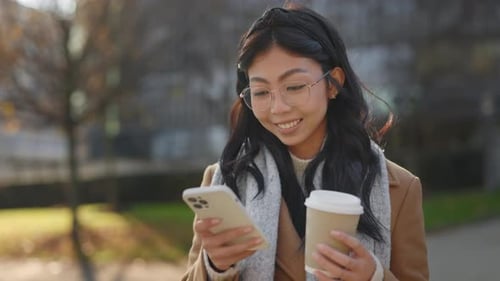 Smiling Woman Using Phone Holding Coffee