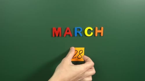 Hand sticking a sticker 28 March calendar day on school board. 28 date of March. Twenty eighth day