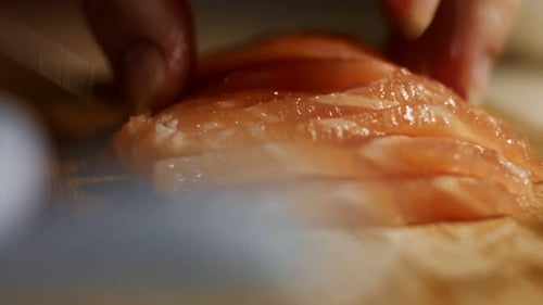 Closeup of Female Hand Slicing Fresh Salmon Fillet on a Wooden Board