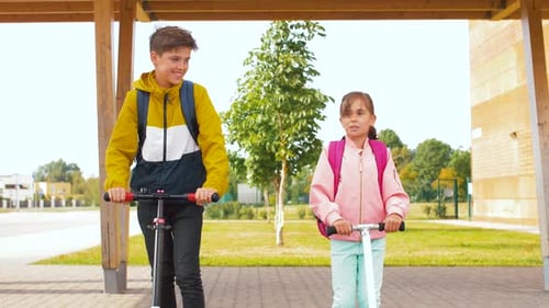 Happy school children with backpacks enjoying scooter ride outdoors in spring