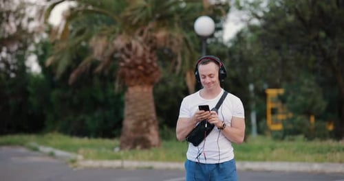 Handsome Man Listening Music in Headphones Walking at Summer City