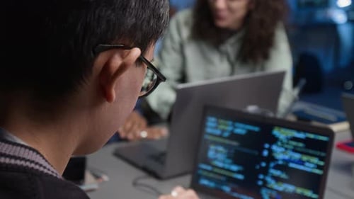 Dark-Haired IT Specialist Writing Code on Laptop Working in Office at Night