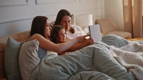 Family Relaxing Together with Tablet in Bed