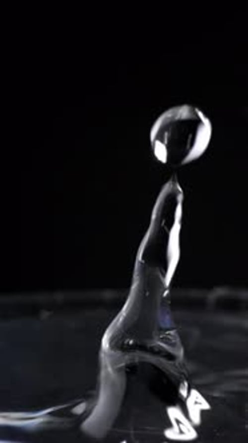Vertical view, drops of water fall into a full glass splashing with back minimal background, close u