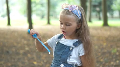 Little Happy Child Girl Blowing Soap Bubbles Outdoors in Summer Park