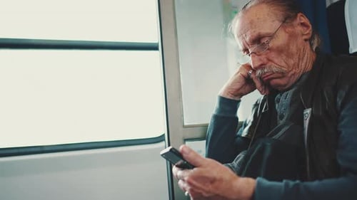 Une personne âgée portant des lunettes utilise son téléphone portable lors d'un voyage en train