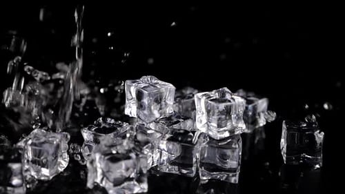 A stream of water falls on ice cubes on a black background. Slow motion.