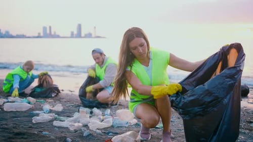 Freiwillige hilft bei Sonnenuntergang, die Küste von Plastikmüll zu reinigen