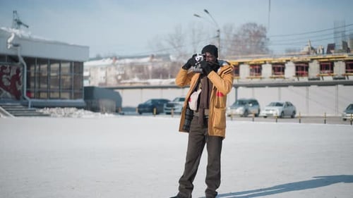Photographer Adjusting Focus and Reviewing Shot on Snowy Street Under Winter Sun