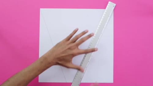 Tracing diagonal lines with ruler and pencil on paper, pink background.
