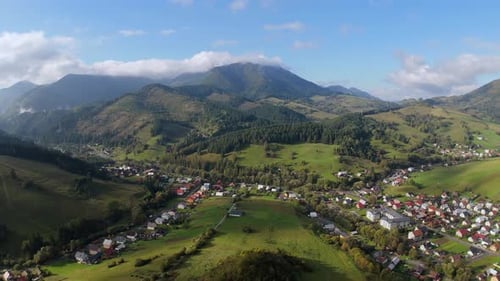 Aerial View of Green Mountain Valley with Village Houses and Forests Under Cloudy Blue Sky