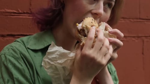Young Adult Eating a Burger Against Brick Wall