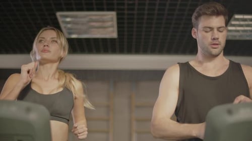 Young Man Drinking Water on Treadmill in Fitness Gym. Beautiful Couple Training