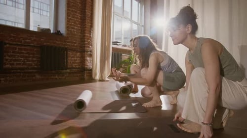 Three Female Yoga Lesson Participants Rolling Out Mats in Sunny Loft Studio