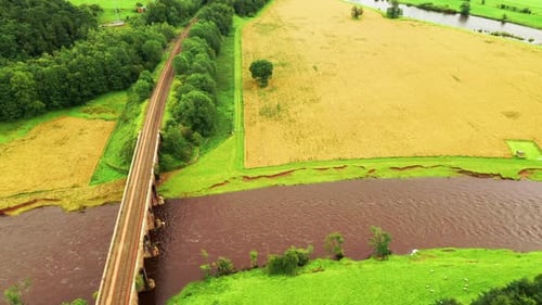 Aerial tracking shot looking over a river flowing under a train viaduct, in the English green countr