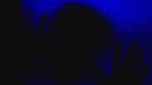 Spine-chilling silhouette of possessed man creeps on glass in the dark under haunting blue light