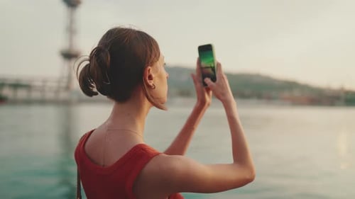Close-up, girl stands on the embankment and takes pictures of sunrise on a mobile phone