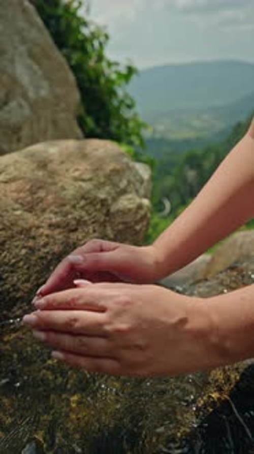 Mãos femininas coletando água cristalina de riacho de montanha sobre rochas naturais Conceito de pureza de água limpa
