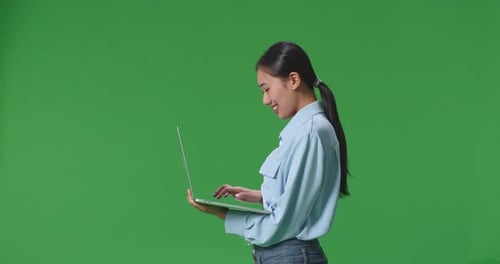 Side View Of Asian Business Woman Using Laptop Computer On Green Screen Background In The Studio