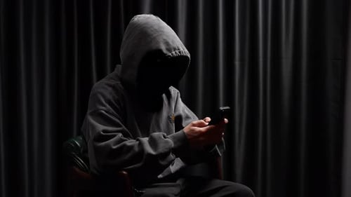 Hooded figure using mobile phone in dark environment