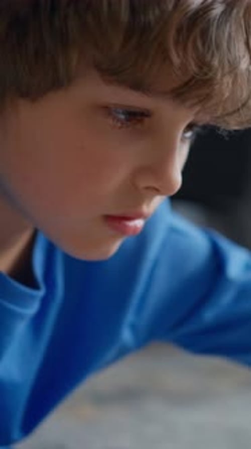 Closeup of a Focused Young Child in a Blue Shirt Drawing with a Pencil on Paper Capturing Quiet
