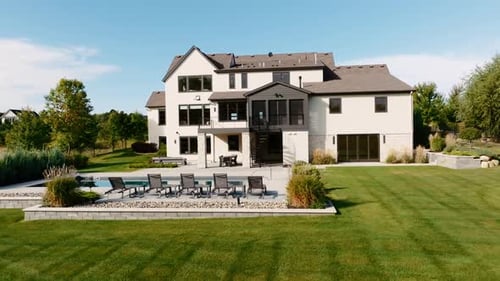 an aerial drone shot of the backyard of a large luxury home with a pool, large backyard, and patio s