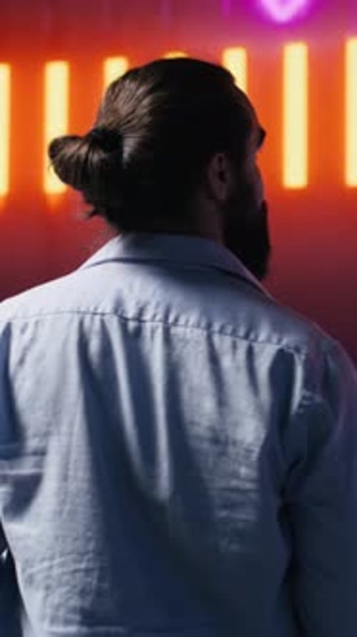 Vidéo verticale Jeune homme décontracté regardant autour de lui les néons lumineux aux couleurs vives