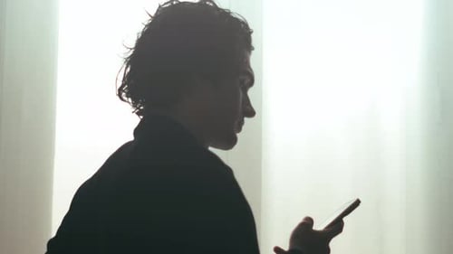 Silhouette of Man with Curly Hair Using Smartphone in Bright Room